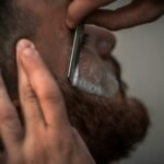 Detailed close-up image of a barber using a razor for precise beard trimming in the barbershop.