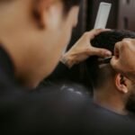 Close-up of a barber expertly styling a man's hair with a razor and comb in a trendy barbershop.
