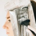 Close-up of a woman getting hair highlights with foil and dye brush.